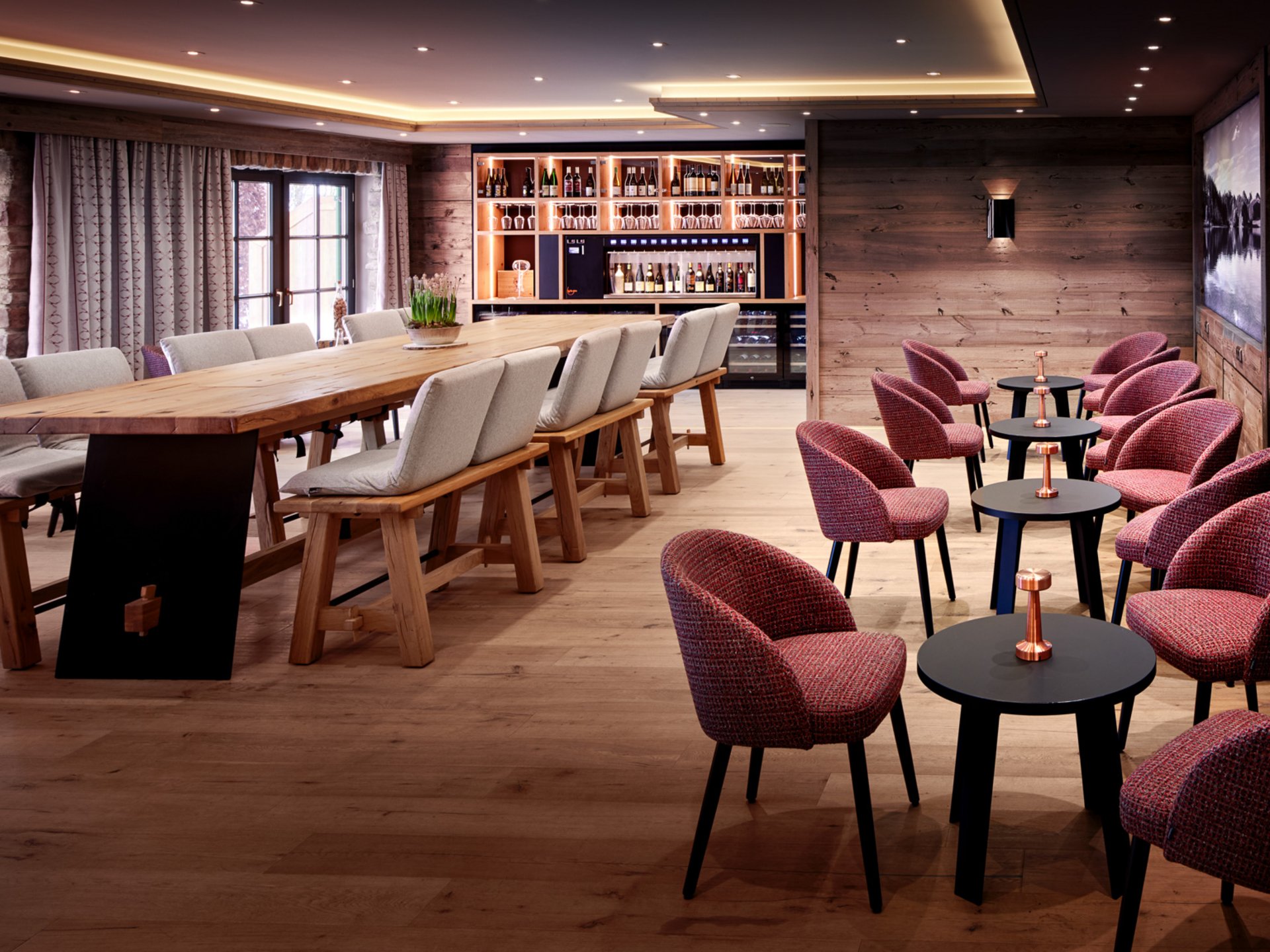 Wellnesshotel in Füssen im Allgäu | Hotel Sommer Moderner Lounge-Bereich mit Holztischen, bequemen Stühlen und Bar im Hintergrund